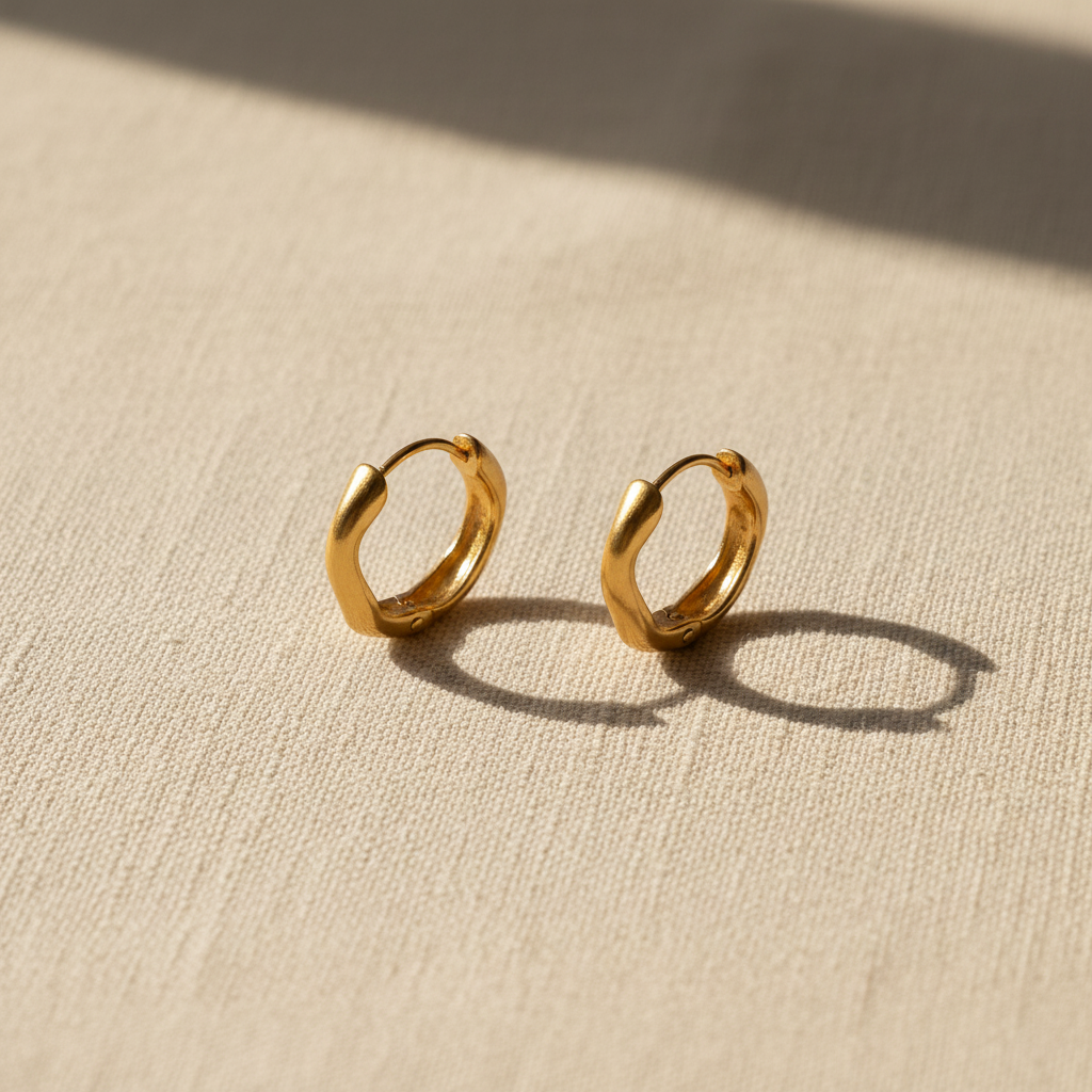 Gold twisted wave hoop earrings on warm cream linen surface