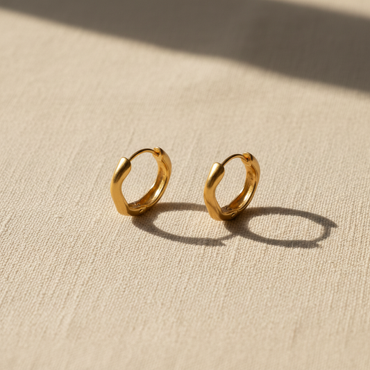 Gold twisted wave hoop earrings on warm cream linen surface
