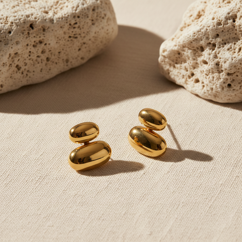 Gold oval bean stud earrings styled on neutral linen